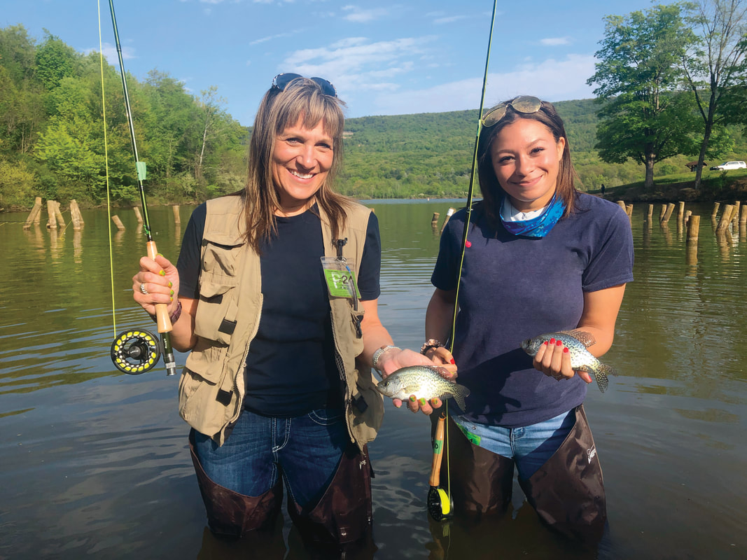 two women standing in water, fishing with fish in hand